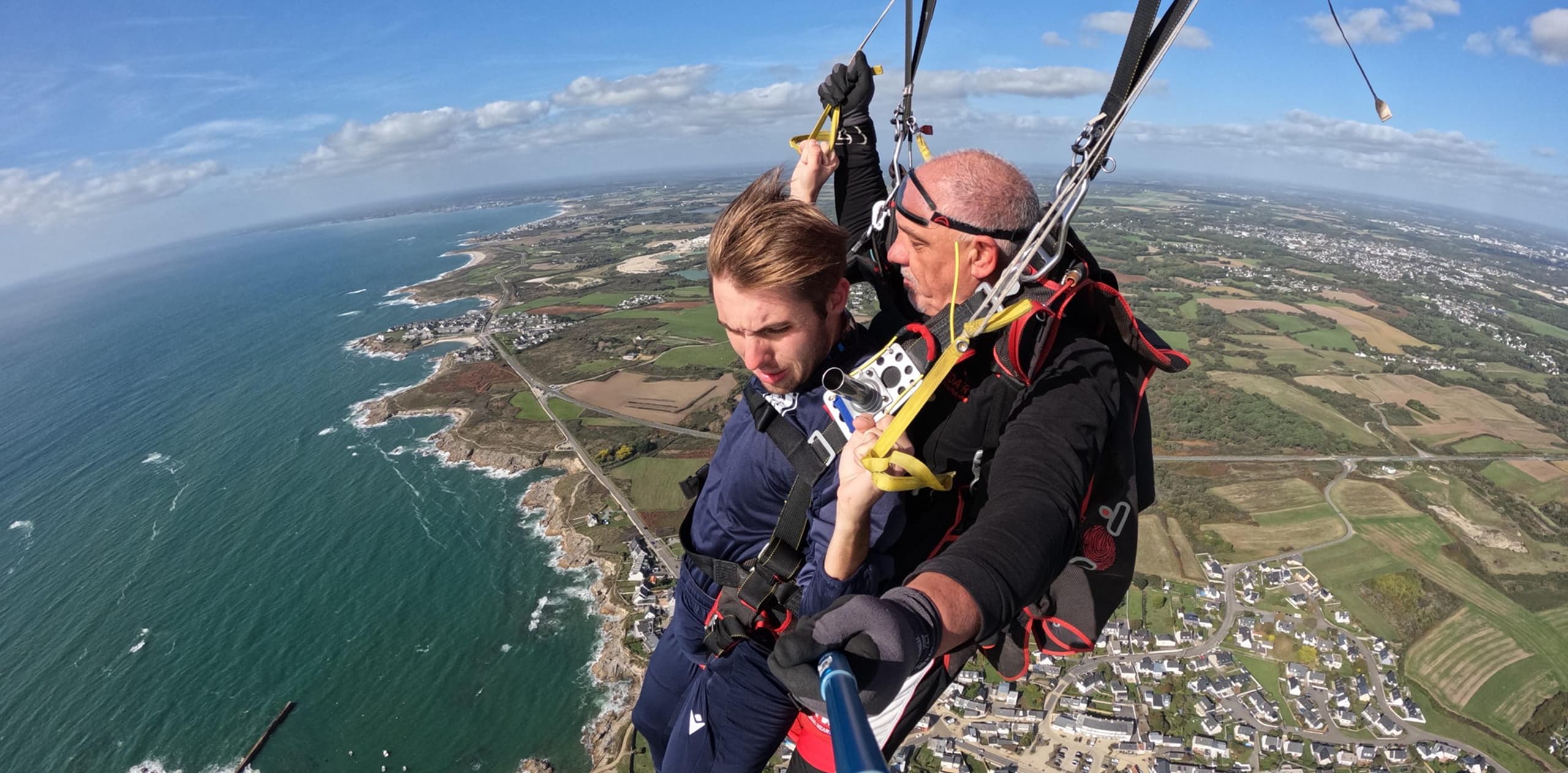 Jeune homme en baptême tandem sous voile avec moniteur, vue panoramique sur la côte rocheuse bretonne de Péréllo-Plages et ses champs verdoyants – Saut en parachute Bretagne